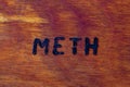 The word meth for Methamphetamine - burned by hand with woodburner on brown wood flat surface Royalty Free Stock Photo