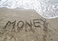 Word MONEY written on the sand and the wave that is erasing the