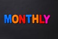 The word MONTHLY written in letters of the children`s magnetic alphabet on a black Royalty Free Stock Photo