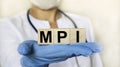 Word MPI on wooden cube blocks in the hands in protective gloves of a doctor woman. Blurring doctor on background