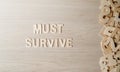 The word MUST SURVIVE, Wooden letters on a wooden table.