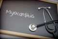 Word Myocarditis written in chalk on a blackboard black next to a stethoscope