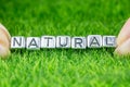 Word NATURAL written in metal letters laid on grass and held between the fingers of a woman. Concept of wellness background Royalty Free Stock Photo