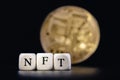 The word NFT is laid out of cubes with letters on background golden cryptocoin