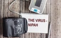 The word about the Nipah virus on a notepad, next to a blood pressure monitor on a wooden background