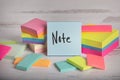 The word note hand written on blue posted note sticky notes stacked and piled on colorful cards