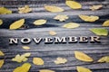 Word November, wooden letters. Frame of yellow leaves, wooden background