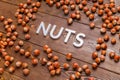 the word nuts laid with silver letters on wooden board background surrounded with scattered hazelnuts Royalty Free Stock Photo