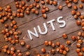 the word nuts laid with silver letters on wooden board background surrounded with scattered hazelnuts Royalty Free Stock Photo