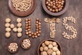 Word nuts from various type of nut. Walnut, hazelnut, almond, pistachio on brown abstract background, top view, flatlay Royalty Free Stock Photo