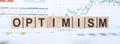 Word OPTIMISM made with wood building blocks on background from financial graphs and charts Royalty Free Stock Photo