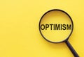 The word OPTIMISM is written on a magnifying glass on a yellow background Royalty Free Stock Photo