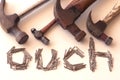 Word `ouch` with four old hammers and small nails acts as a warning to be careful.