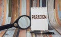 The word paradigm is written on a white notebook, near a pen and a magnifying glass Royalty Free Stock Photo
