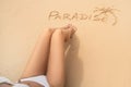 Word paradise and one palm on the sandy beach near the women`s legs. Summer vacation concept. Realax Royalty Free Stock Photo
