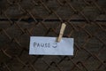 Word pause is written in English on a sheet of white paper hanging on the fence on the filler