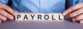 The word PAYROLL is made up of wooden cubes by a man. Business concept