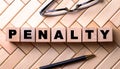 The word PENALTY is written on wooden cubes on a wooden background next to a pen and glasses