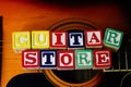 Word or phrase Guitar Store made with letter cubes, standing on guitar.