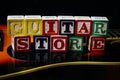 Word or phrase Guitar Store made with letter cubes, standing on guitar.