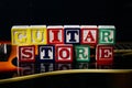 Word or phrase Guitar Store made with letter cubes, standing on guitar.