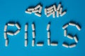 The word Pills is lined with white capsule tablets on a blue Royalty Free Stock Photo