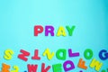 Word PRAY made of colorful letters on blue background.