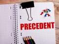 The word PRECEDENT is written in a notebook near multi-colored pencils and buttons on a wooden background Royalty Free Stock Photo