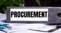 The word PROCUREMENT is written on a gray file folder next to documents. Business concept