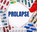 The word PROLAPSE is written on a light background surrounded by multi-colored packages with pills. Medical concept