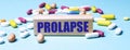 The word PROLAPSE is written on a wooden block on a light blue background among multi-colored pills. Medical concept