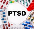 The word PTSD is written on a light background surrounded by multi-colored packages with pills. Medical concept