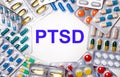 The word PTSD is written on a light background surrounded by multi-colored packages with pills. Medical concept