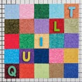 The word quilt composed of colored wooden letters laid out on colorful pieces of fabrics arranged in shape of square