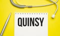 The word qUINSY written on a white notepad on a yellow background