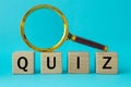 Word Quiz written on wooden blocks and a magnifying glass on a blue background, concept of questions and answers in game shows