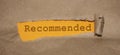 The word Recommended appearing on mustard yellow paper behind torn brown paper