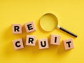 The word recruit on wooden cubes with a magnifying glass. Recruitment, employment, candidate search and job hiring business