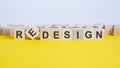 the word redesign is made of wooden cubes lying on a yellow table. one of the cubes is placed on an edge, concept Royalty Free Stock Photo