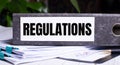 The word REGULATIONS is written on a gray file folder next to documents. Business concept