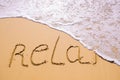 Word Relax hand written in the sand with a sea wave. Close up sand texture on beach in summer Royalty Free Stock Photo