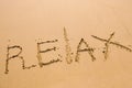 Word Relax hand written in the sand with a sea wave. Close up sand texture on beach in summer