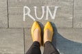 Word run written on gray pavement with woman legs, view from above