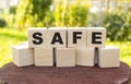 The word SAFE is made up of wooden cubes lying on an old tree stump against a blurred garden background