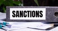 The word SANCTIONS is written on a gray file folder next to documents. Business concept