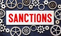 The word sanctions is written on a stationery tablet that lies on a financial document near a blue notebook.