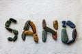 Word SAND is written using colored stones on a white sandy surface