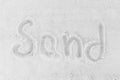 The word sand is written on a white beach sand background. Sign or symbol of sand concept