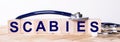 The word SCABIES is written on wooden cubes near a stethoscope on a wooden background. Medical concept