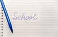 The word school written in blue pen on a notebook with lines and a blue pen.